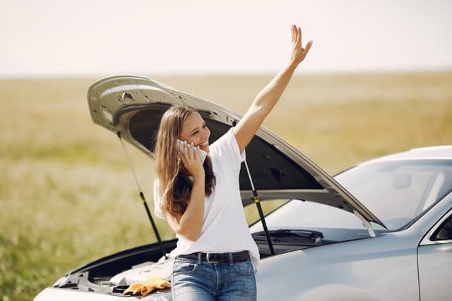 Vrouw naast een auto met pech die de verzekering belt